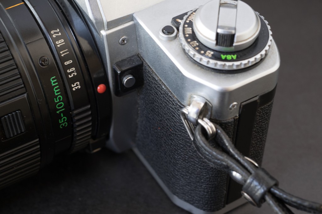Canon AV-1 - the button on the top plate is the battery check. The button on the side of the reflex chamber is for exposure compensation
